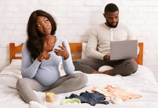 Hermosa mujer embarazada preparando ropa de bebé, marido usando el ordenador portátil — Foto de Stock