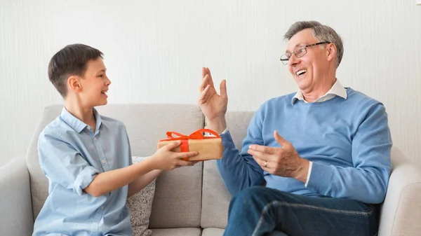 Внук поздравляет дедушку с подарочной упаковкой, сидя на диване, Панорама — стоковое фото