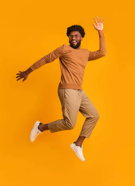 Χαρούμενος τύπος με γυαλιά πηδάει πάνω από πορτοκαλί φόντο — Φωτογραφία Αρχείου