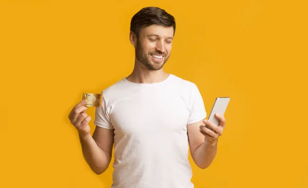 Fröhlicher Mann mit Smartphone und Kreditkarte im Stehen, Studioaufnahme — Stockfoto