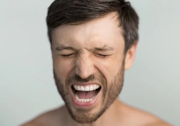 Portret van een man van middelbare leeftijd die schreeuwt met gesloten ogen, grijze achtergrond — Stockfoto