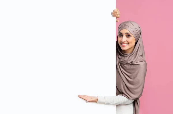 Красива мусульманська дівчина в хіджабі вказує на білу порожню рекламну дошку — стокове фото