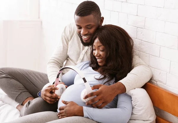 Mulher grávida e seu marido colocando fones de ouvido em sua barriga — Fotografia de Stock