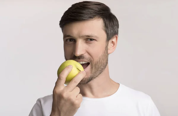 Homem feliz mordendo maçã em pé sobre fundo de estúdio branco — Fotografia de Stock