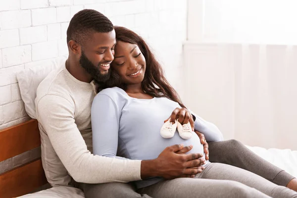 Pregnant couple putting future baby little boots on tummy — Stock Photo, Image