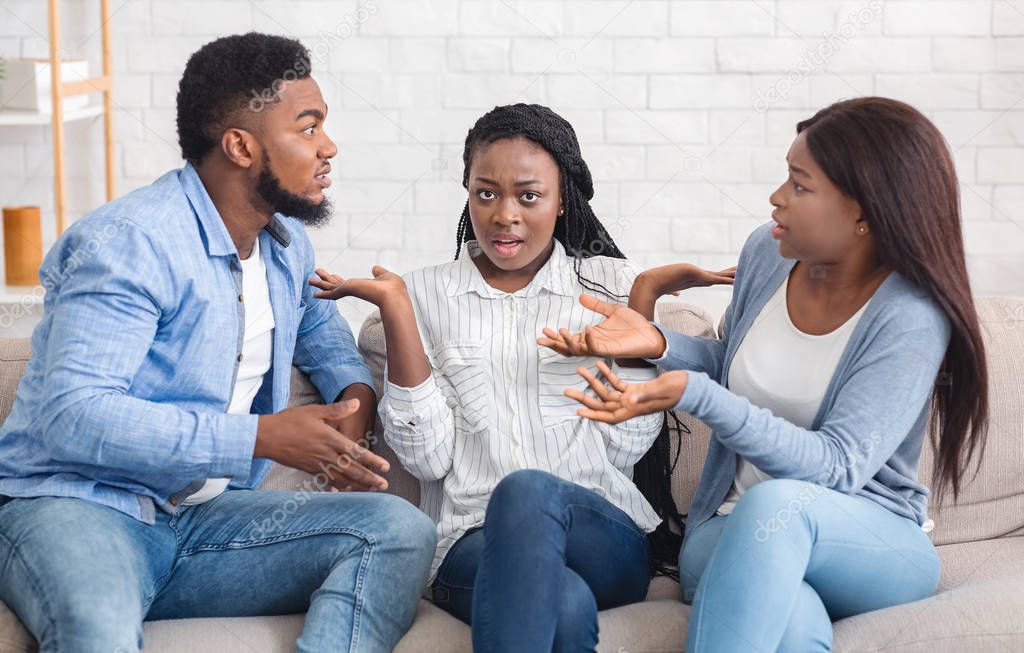 Annoyed black millennial girl sitting between arguing couple