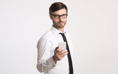 İş adamı elinde telefonla stüdyoda duran kameraya bakıyor.