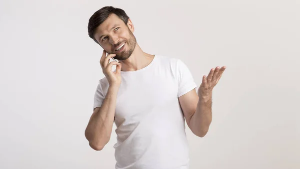Чоловік розмовляє на мобільному телефоні жестикулює і посміхається на білому тлі — стокове фото