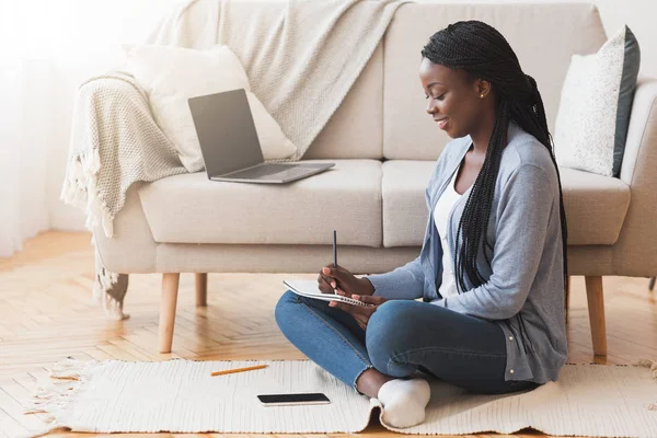 Studentessa nera che prende appunti mentre studia a casa con il computer portatile — Foto Stock