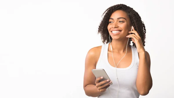Sonriente chica afroamericana usando el teléfono para escuchar música — Foto de Stock