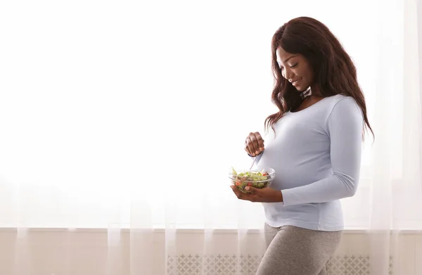 Wanita hamil makan salad segar di samping jendela di rumah — Stok Foto