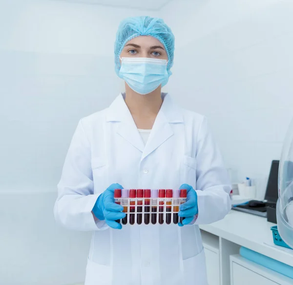 Женщина в медицинской одежде держит кровь в пробирках в лаборатории — стоковое фото