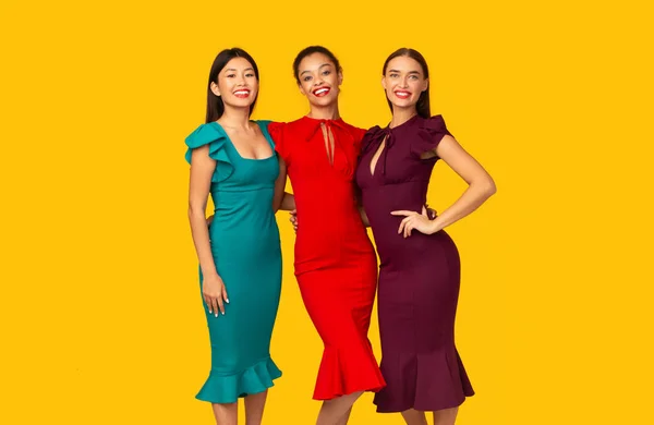 Três modelos multirraciais em vestidos em pé sobre fundo estúdio amarelo — Fotografia de Stock