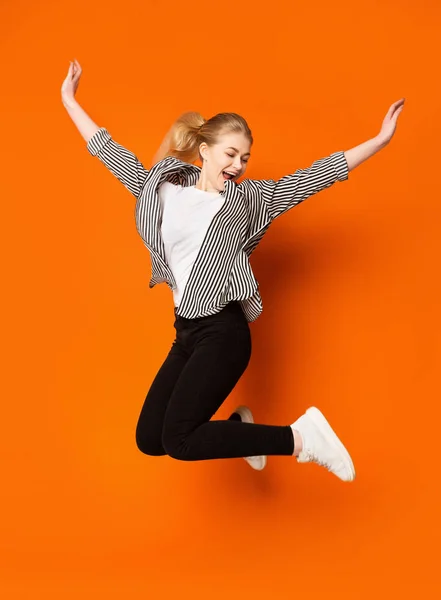 Euphoric teen girl jumping over orange studio background — 图库照片