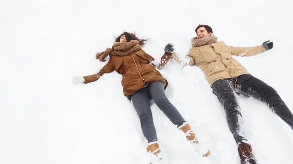 Pareja feliz acostada en la nieve riendo sosteniendo las manos al aire libre, Panorama —  Fotos de Stock