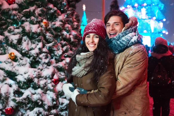 Couple Hugging Next To Decorated Christmas Tree In Night City