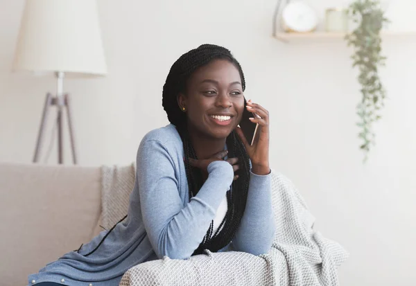 Fröhliches schwarzes Mädchen, das auf dem Handy auf der Couch zu Hause sitzt — Stockfoto