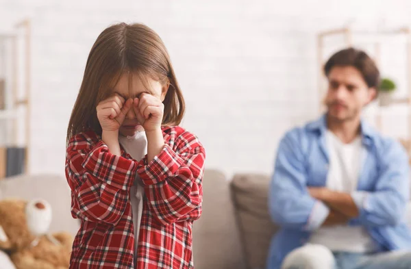 Küçük kız babasıyla kavga ettikten sonra ağlıyor, arkasında kızgın bir baba var.
