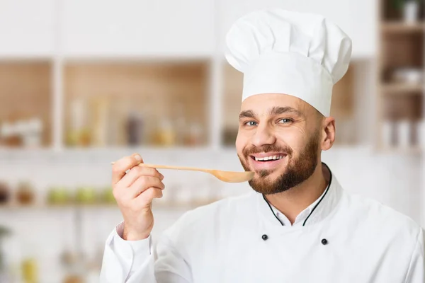 Chef sonriente Hombre degustación de alimentos sosteniendo cuchara en la cocina del restaurante — Foto de Stock