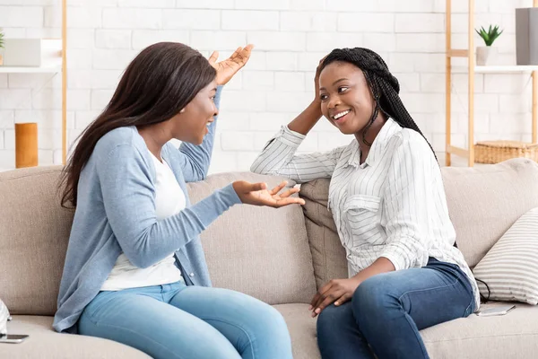 Две черные девушки тысячелетия сидят на диване и болтают — стоковое фото