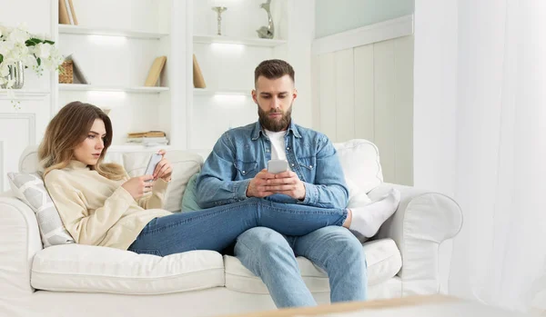 Adicción a Internet. Pareja joven usando teléfonos inteligentes en el sofá —  Fotos de Stock