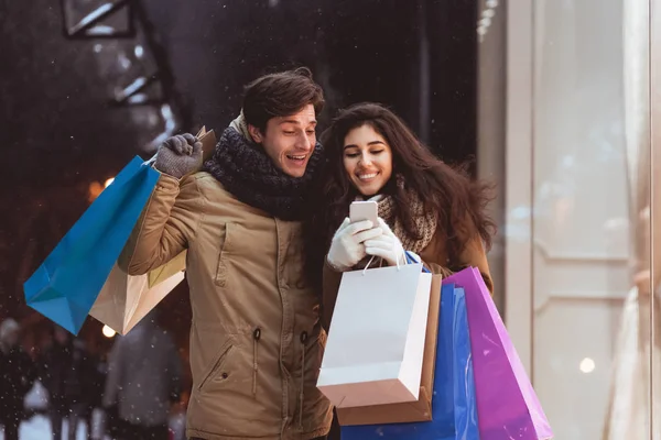 Casal usando Smartphone Segurando Shopper sacos ao ar livre à noite — Fotografia de Stock
