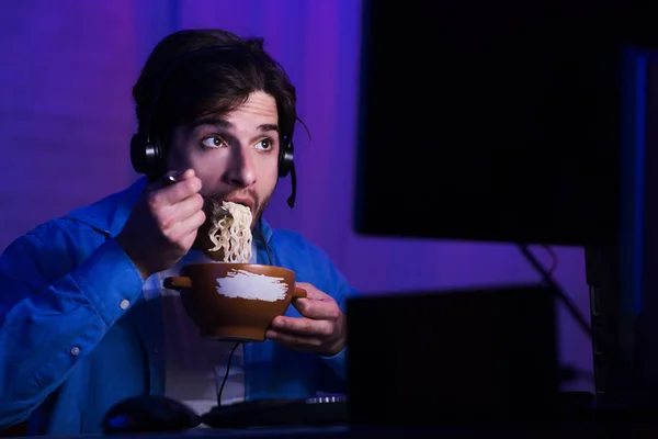 Male gamer eating noodle soup, playing video games — Stock Photo, Image