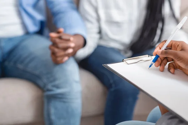 Marriage counselor taking notes during therapy session with black married couple