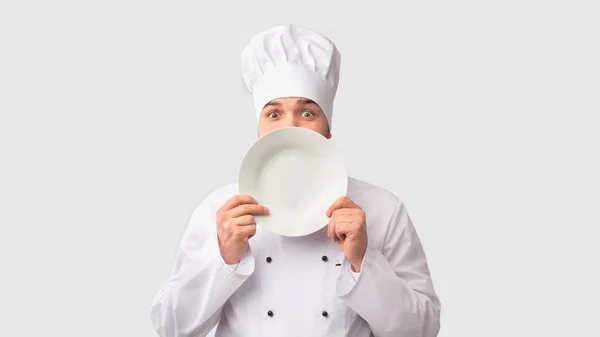 Kuchař drží desku blízko obličeje stojící, bílé pozadí — Stock fotografie