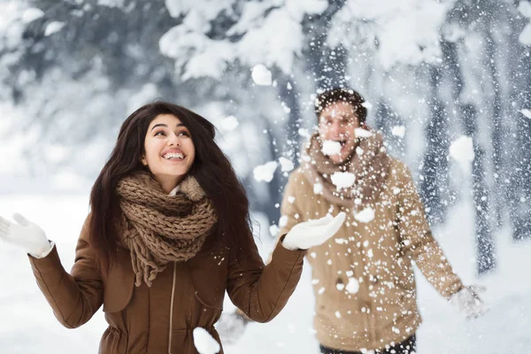 Feliz pareja lanzando nieve caminando en el parque nevado por la mañana —  Fotos de Stock