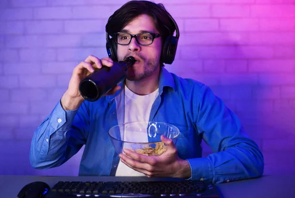 Jogador concentrado bebendo cerveja com chips, olhando para a tela — Fotografia de Stock