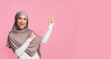 Neşeli Müslüman kadın pembe arka planda fotokopi alanını gösteriyor.