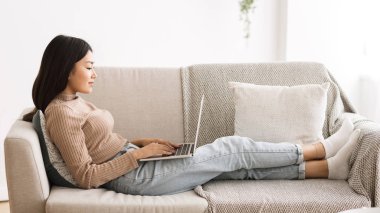 Genç kız dizüstü bilgisayarda sohbet ediyor, kanepede oturuyor.