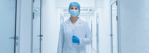 Mujer en ropa médica protectora pasando por un pasillo de laboratorio vacío — Foto de Stock