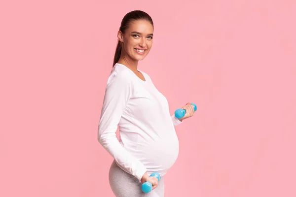 Happy Pregnant Girl Holding Dumbbells Standing On Pink Studio Background — Stok Foto