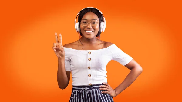 Sorridente afro signora in cuffie wireless gesticolando Victory Sign, Studio — Foto Stock