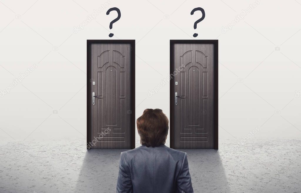 Confused man in suit looking at two similar doors