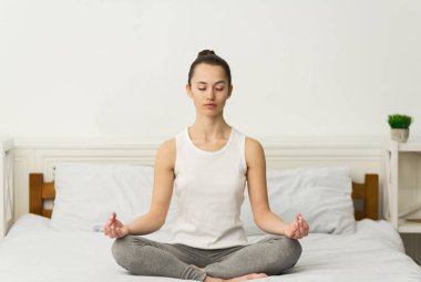Meditasyon. Milenyum kadını yatakta lotus pozisyonunda oturuyor.