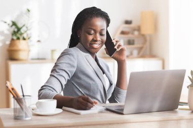 Modern Ofiste telefon görüşmesi yaparken not alan Afro İş kadını