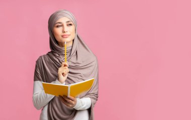 Düşünceli müslüman kız elinde not defteri ve kalemle bir şey düşünüyor.