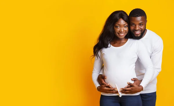 Feliz grávida afro casal abraçando sobre fundo amarelo — Fotografia de Stock