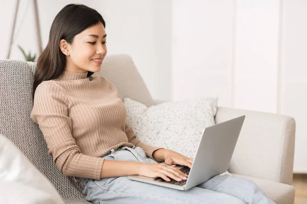 Bastante asiático chica usando laptop, relajante en sofá en casa —  Fotos de Stock