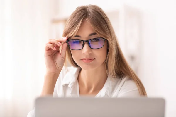 Mujer de negocios en anteojos entrecerrando los ojos trabajando en el ordenador portátil en la oficina —  Fotos de Stock