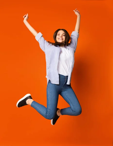 Приголомшлива дівчина-підліток стрибає над помаранчевим студійним фоном — стокове фото