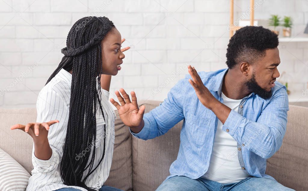 Black millennial couple arguing on sofa at home