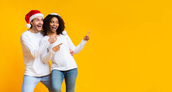 Happy spouses in santa hats pointing with fingers at copy space