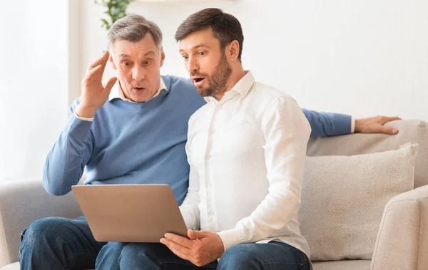 Shocked elderly man and adult son using laptop sitting indoor — Stock Photo, Image