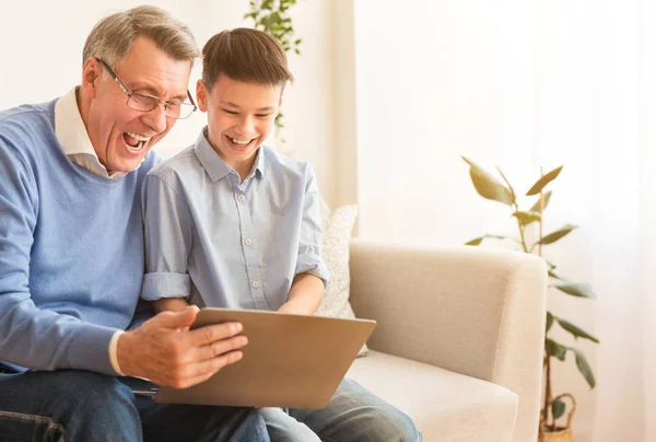 Радісний дідусь і хлопчик використовуючи ноутбук сміється сидячи вдома — стокове фото