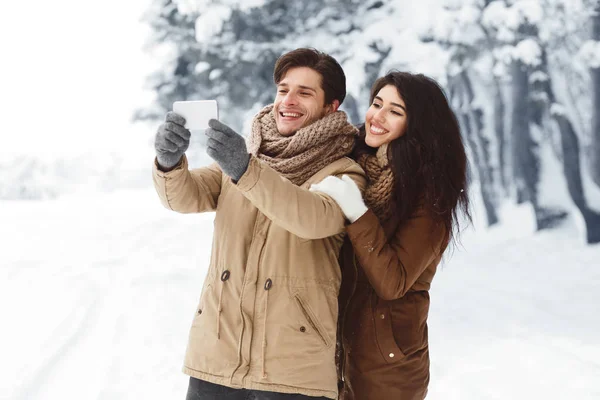 Älskande par gör selfie på telefon stående i snöig skog — Stockfoto