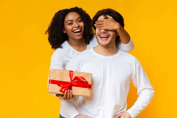 Allegro afro ragazza coprendo i suoi fidanzati occhi e dandogli presente — Foto Stock